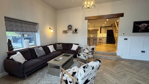Una sala de estar moderna con un sofá modular, una mesa de centro, una alfombra estampada, un sillón de cuero y una cocina visible a través de un umbral abierto.
