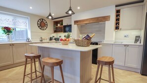Una cocina moderna con una isla central, taburetes de madera, iluminación colgante y un reloj en la pared.