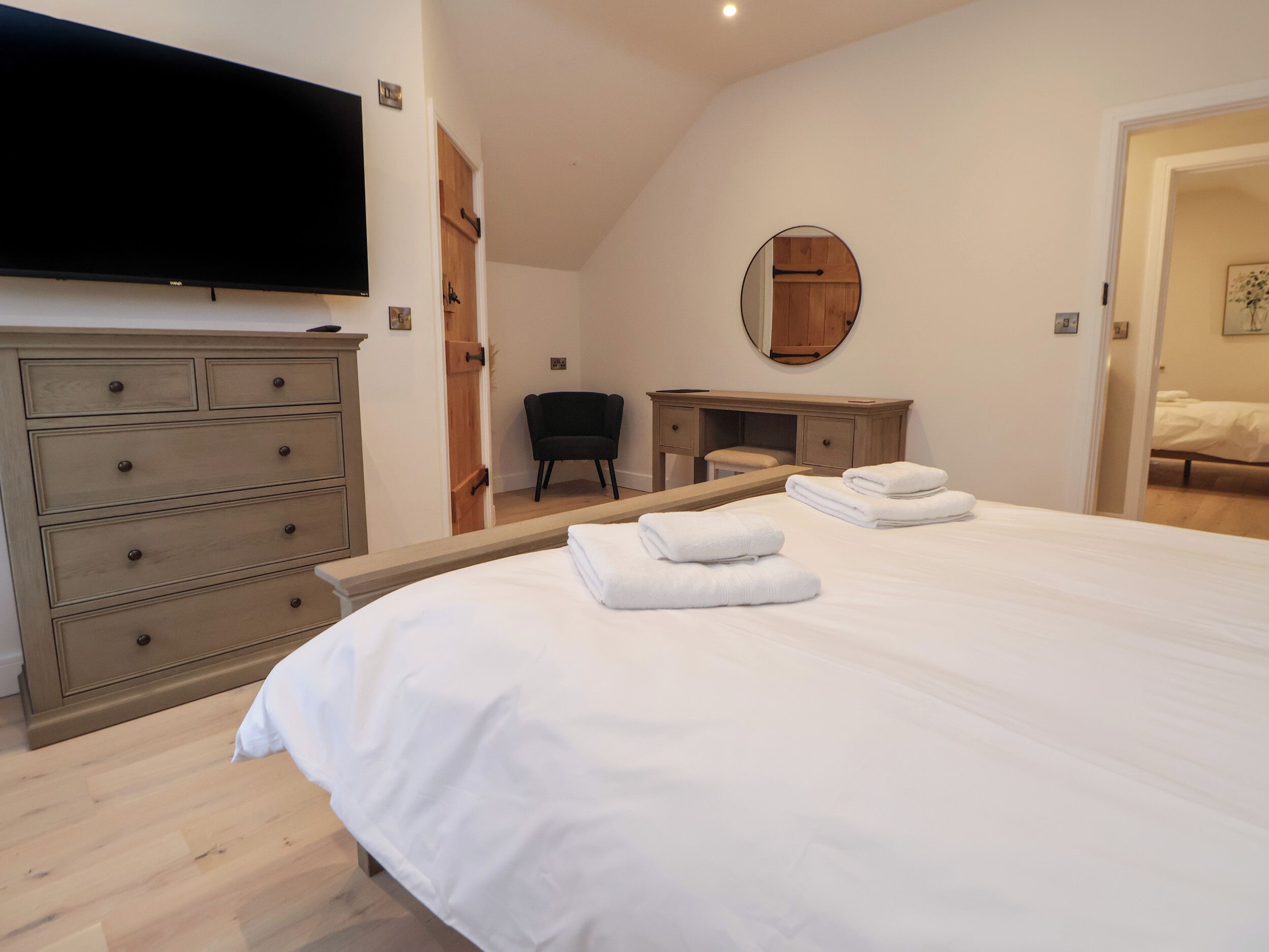 A bedroom with a large bed, a dresser, a desk, a chair, and a television.