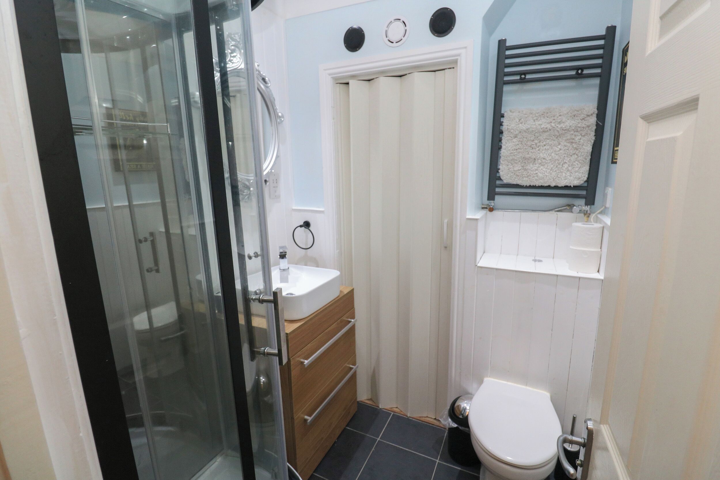 Ein kleines Badezimmer mit Duschkabine aus Glas, weißer Toilette und einem kleinen Waschbecken mit Holzunterschrank.