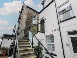 Un escalier menant à un deuxième étage, doté d’une rampe en verre, d’un mur extérieur blanc et d’une fenêtre avec des stores.
