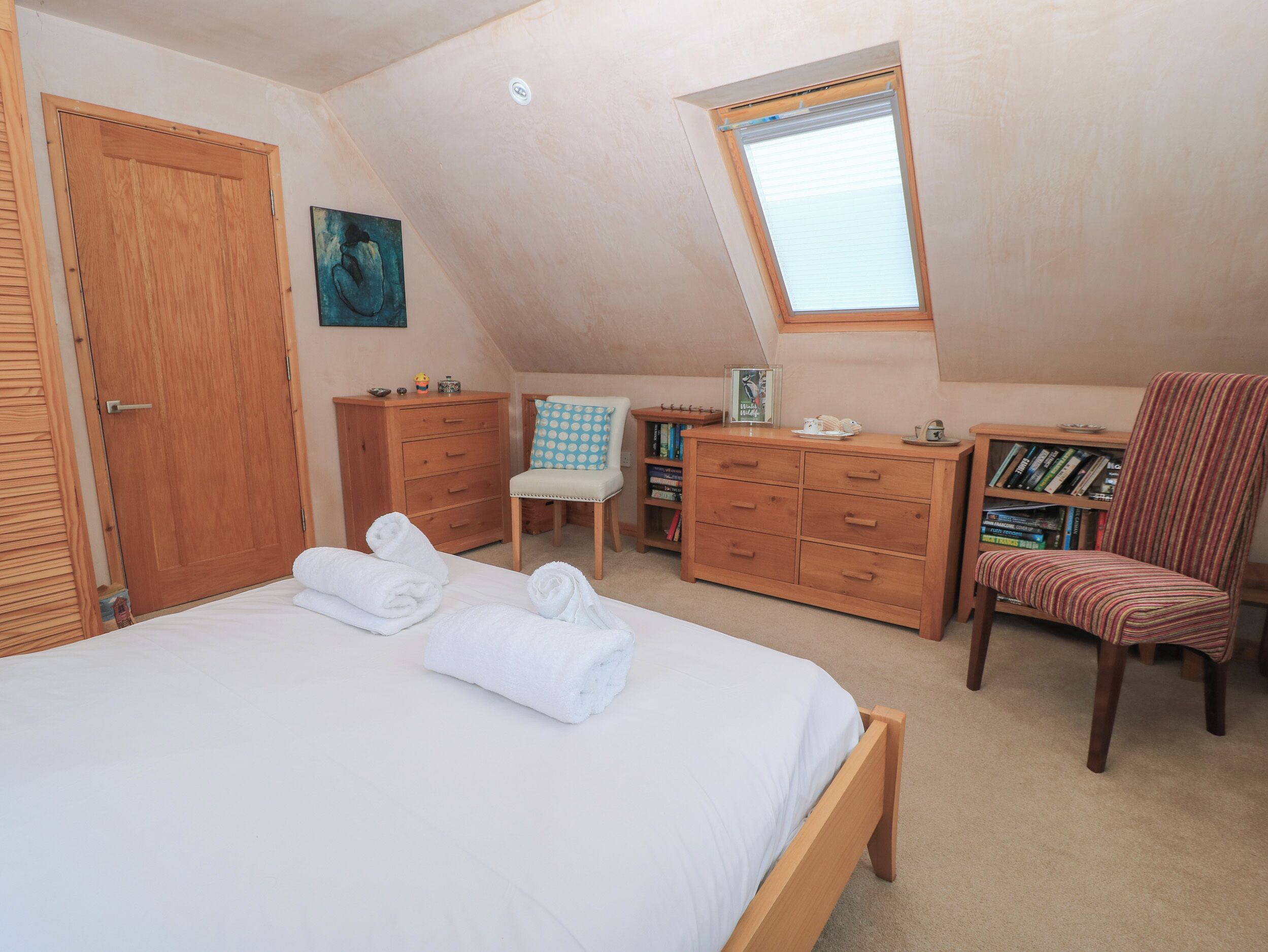 A bedroom with a bed, a wooden dresser, a chair, a bookshelf, and a window.