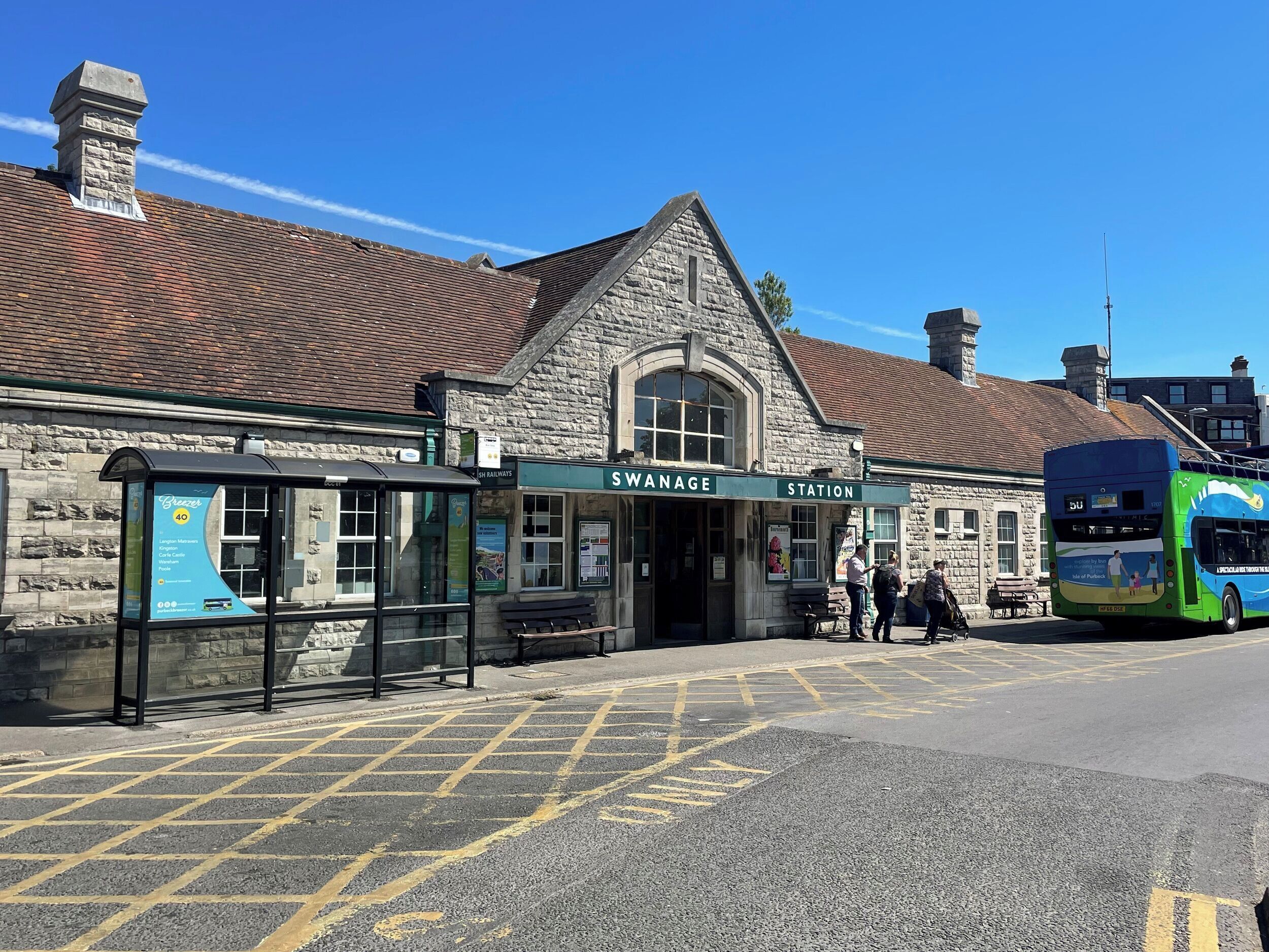 A station building with a stone facade, a bus stop, and a bus parked outside.