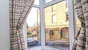 A room with a window overlooking a stone building, a bench with cushions, and curtains. - 5 Hamilton Terrace (Harrogate)