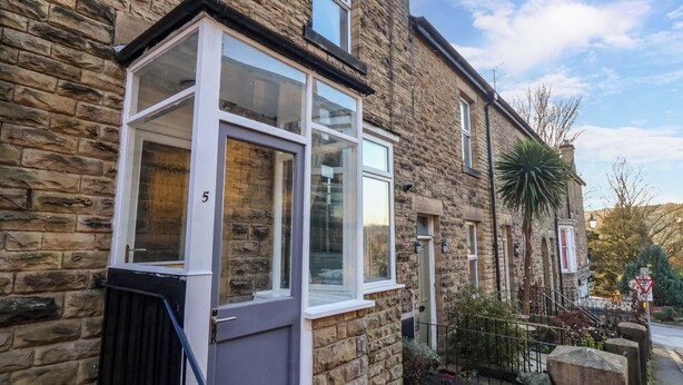A stone house with a large window and a door, a small garden with flowers, and a street sign. - 5 Hamilton Terrace (Harrogate)