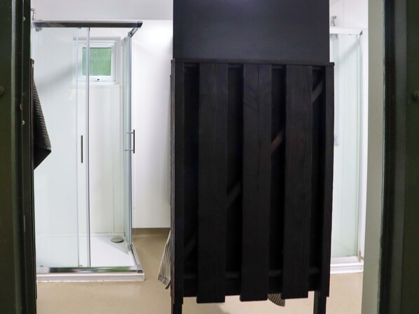 A room with a glass door leading to a shower area, a black piece of furniture, and a white wall. - Ballybeg Pod 5 (Ballybeg)