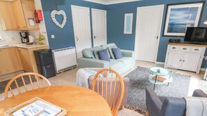 A cozy living space with a dining area, a sofa, a TV, and a kitchen area. - Chy Lowena (Falmouth)