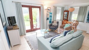A living room with a sofa, a television, a dining table, and a chair. - Chy Lowena (Falmouth)