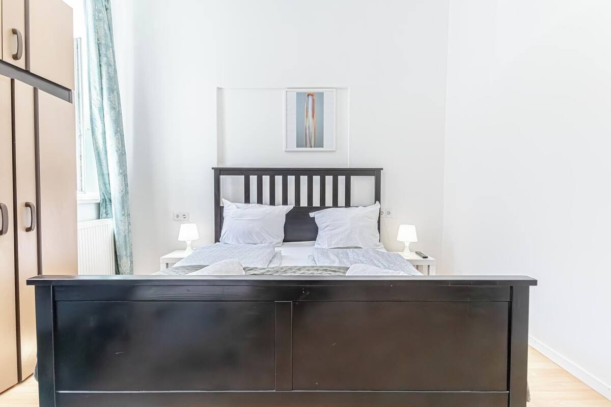 A neatly made bed with white bedding, a dark wooden headboard, and two bedside lamps.