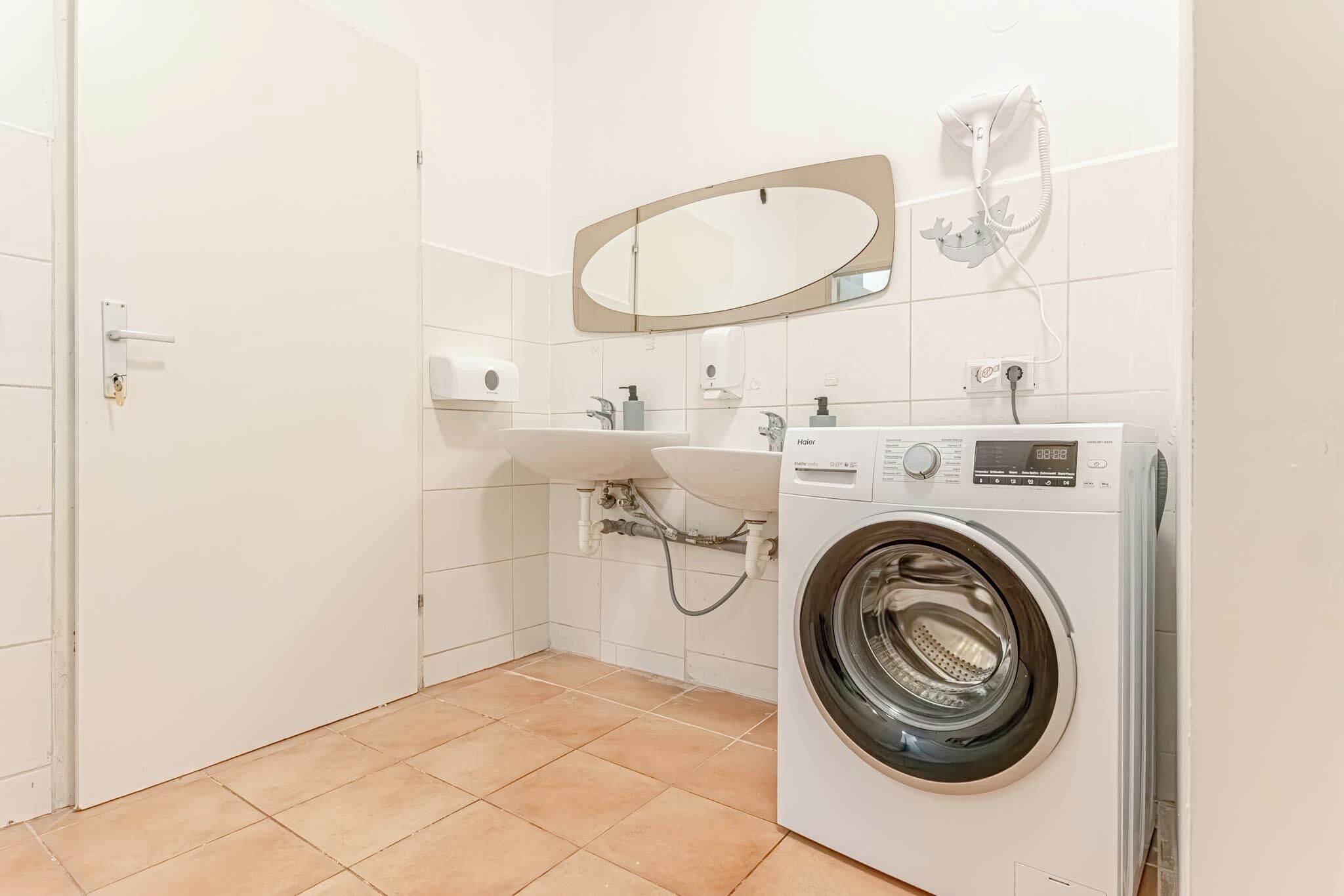 A clean, modern bathroom with a washing machine, a sink, and a mirror.