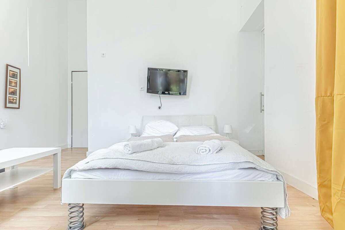 A modern bedroom with a white bed, a mounted TV, and a bench.