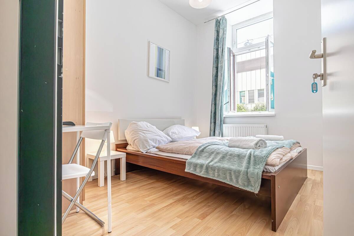 A modern bedroom with a wooden bed, a white desk, and a window with curtains.