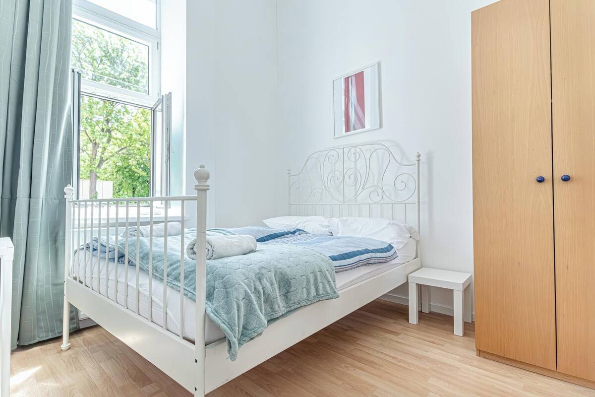 A bedroom with a single bed, a wooden wardrobe, a small bedside table, and a window with curtains.