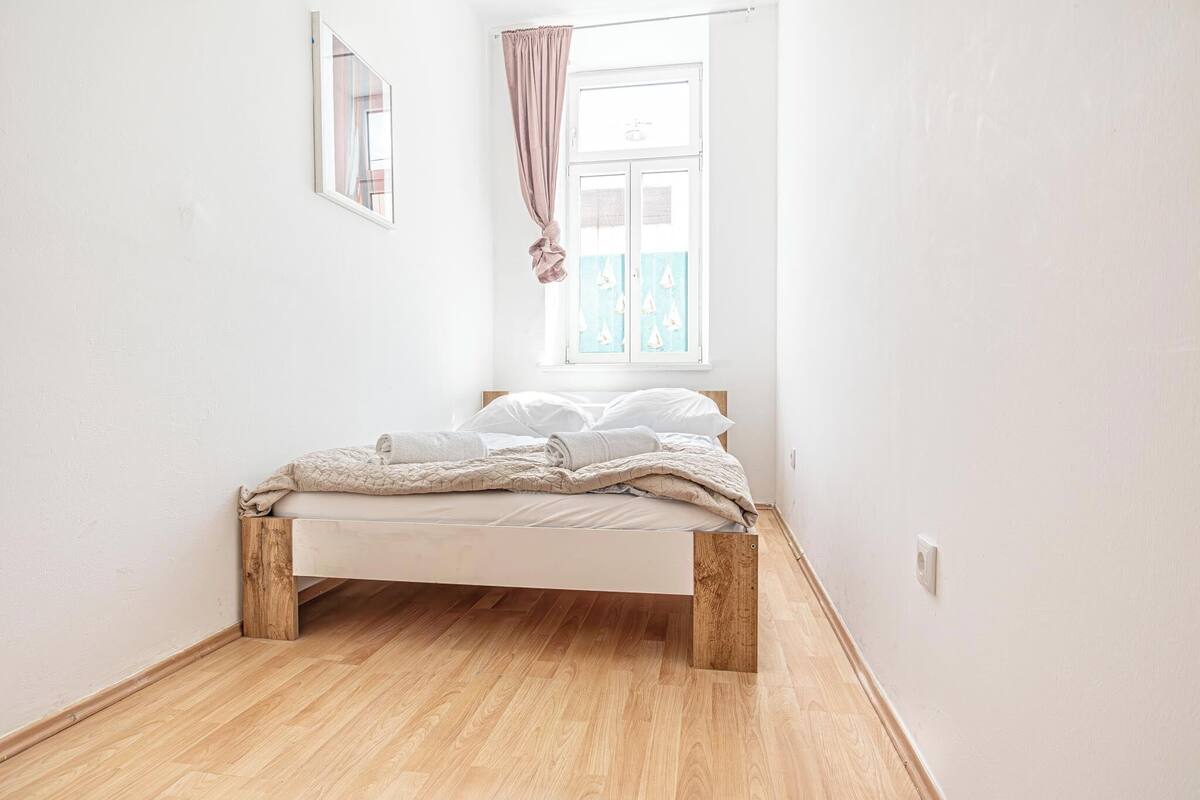 A bedroom with a wooden bed frame, white bedding, and a window with curtains.