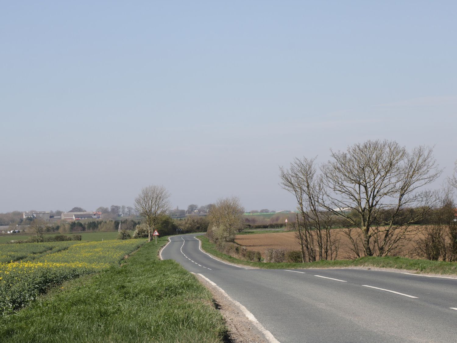 A rural road curving through fields with a clear sky.