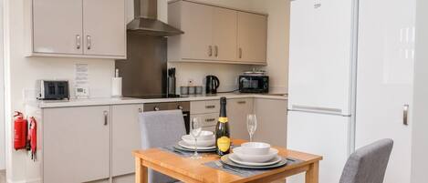 A modern kitchen with a dining table set for two, equipped with a microwave, toaster, and a range hood.