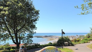 Vista costera con un banco de mosaicos, una señalizadora y un sendero que lleva a la playa.
