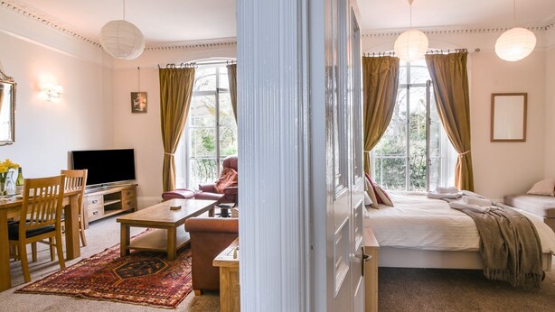 Habitación bien iluminada con cama, escritorio, televisor y ventana con cortinas.