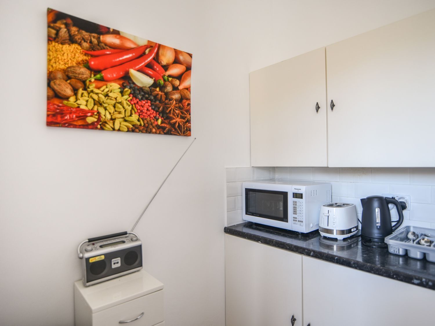 A kitchen with white cabinets, a microwave, a toaster, a kettle, and a radio on a small table.