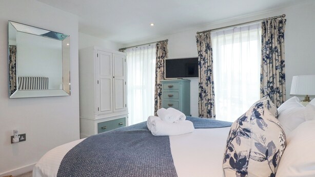 A hotel room with a bed, a mirror, a wardrobe, a television, and floral curtains. - The Trick (St Ives)
