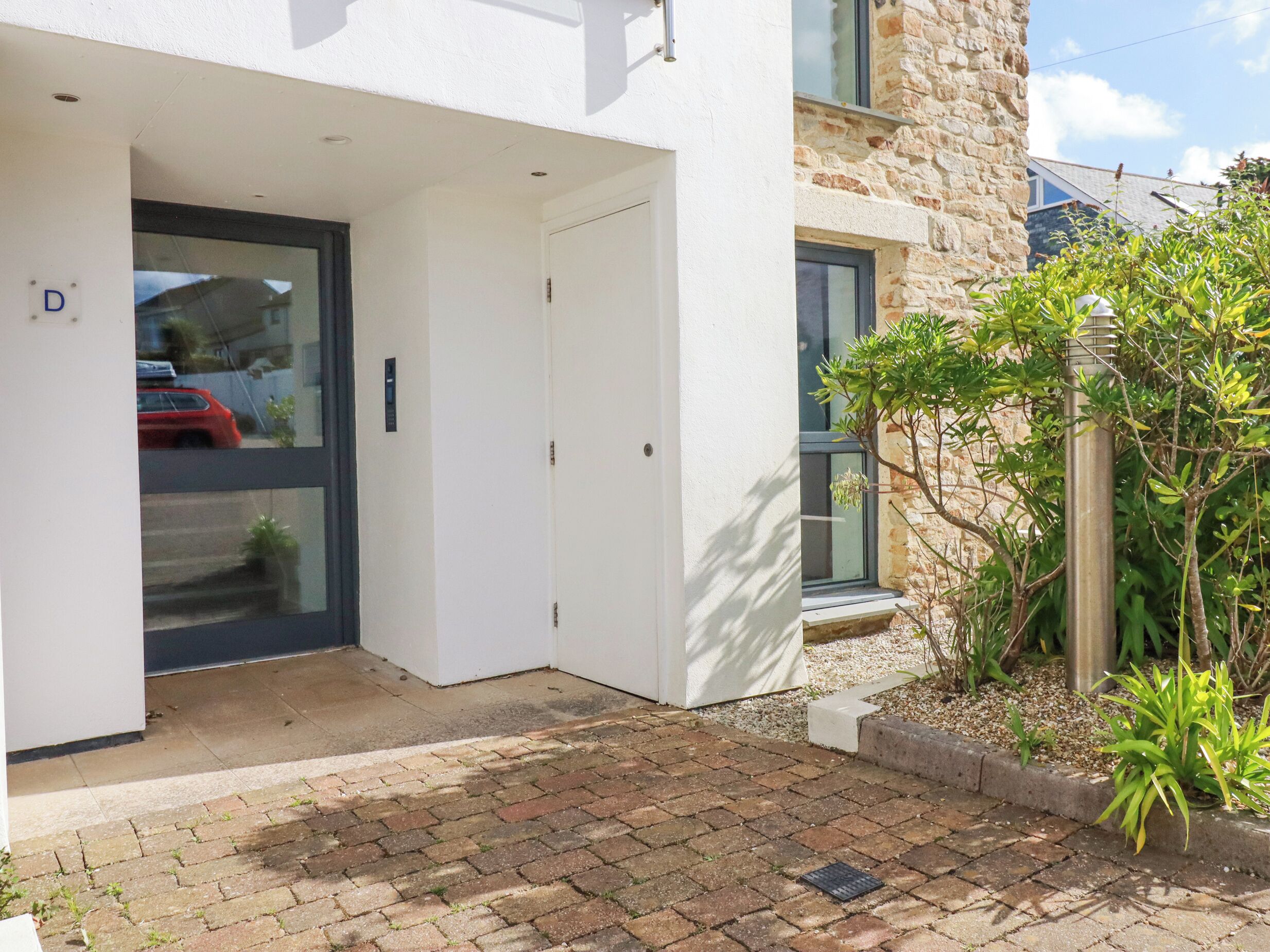 A modern building with a white exterior, a glass door, and a small garden area with plants and a metal structure.