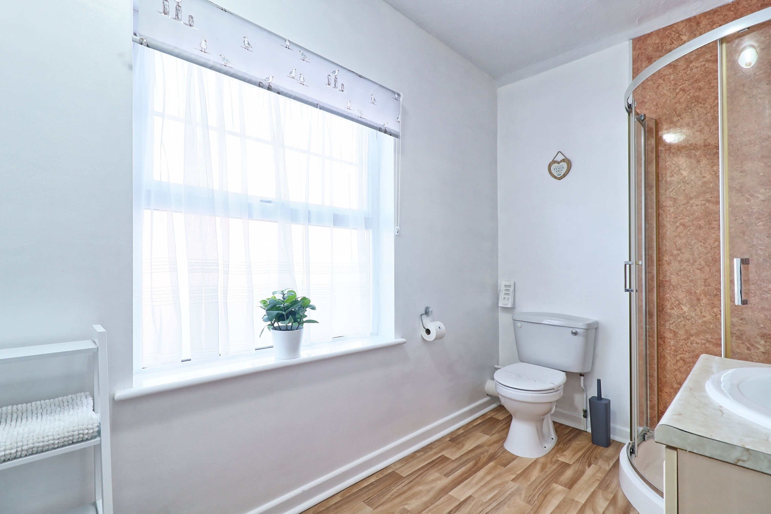 A bathroom with a toilet, a sink, a shower, and a window with a curtain.