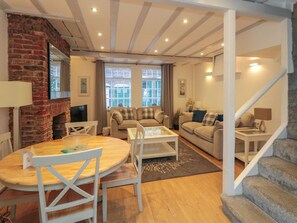 A cozy living room with a brick fireplace, a dining area with a round table and chairs, and a staircase leading to another level.
