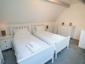 A bedroom with two single beds, a nightstand with a lamp, a dresser, and a framed picture on the dresser.