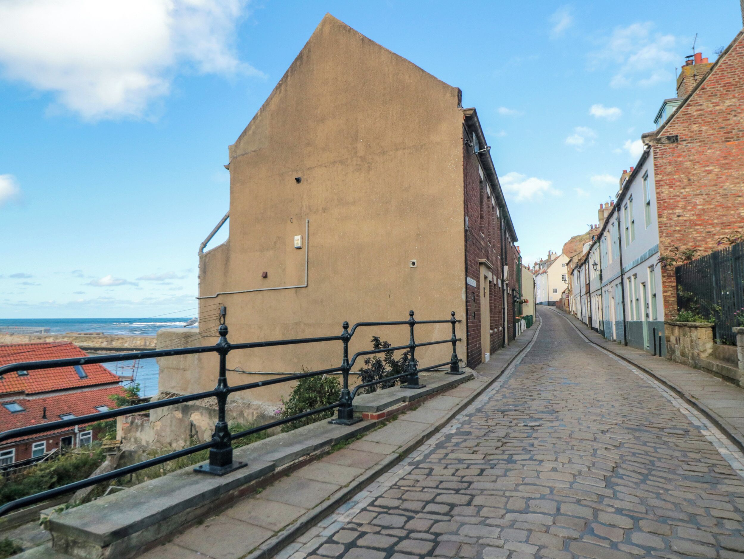 A cobblestone street with a brick building on the left and a row of traditional houses on the right.