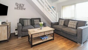 Ein Wohnzimmer mit zwei grauen Sofas, einem Holztisch und einer Treppe mit weißen Geländern.