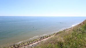 Ein Küstenblick mit blauem Himmel, ruhiger See und einer grasbewachsenen Böschung mit einem Holzsteg.
