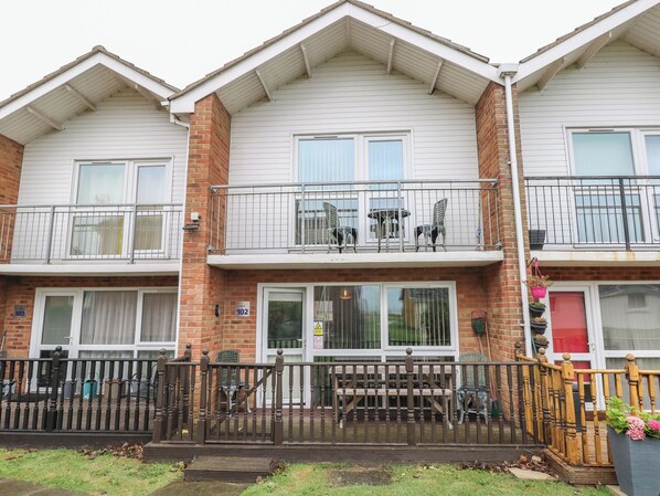 A two-story residential building with a balcony on the upper floor, a front gate, and a small garden area. - 102 Waterside Park (Lowestoft)