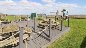 Ein Spielplatz mit Holzspielgeräten, Picknicktischen und einem umzäunten Bereich.