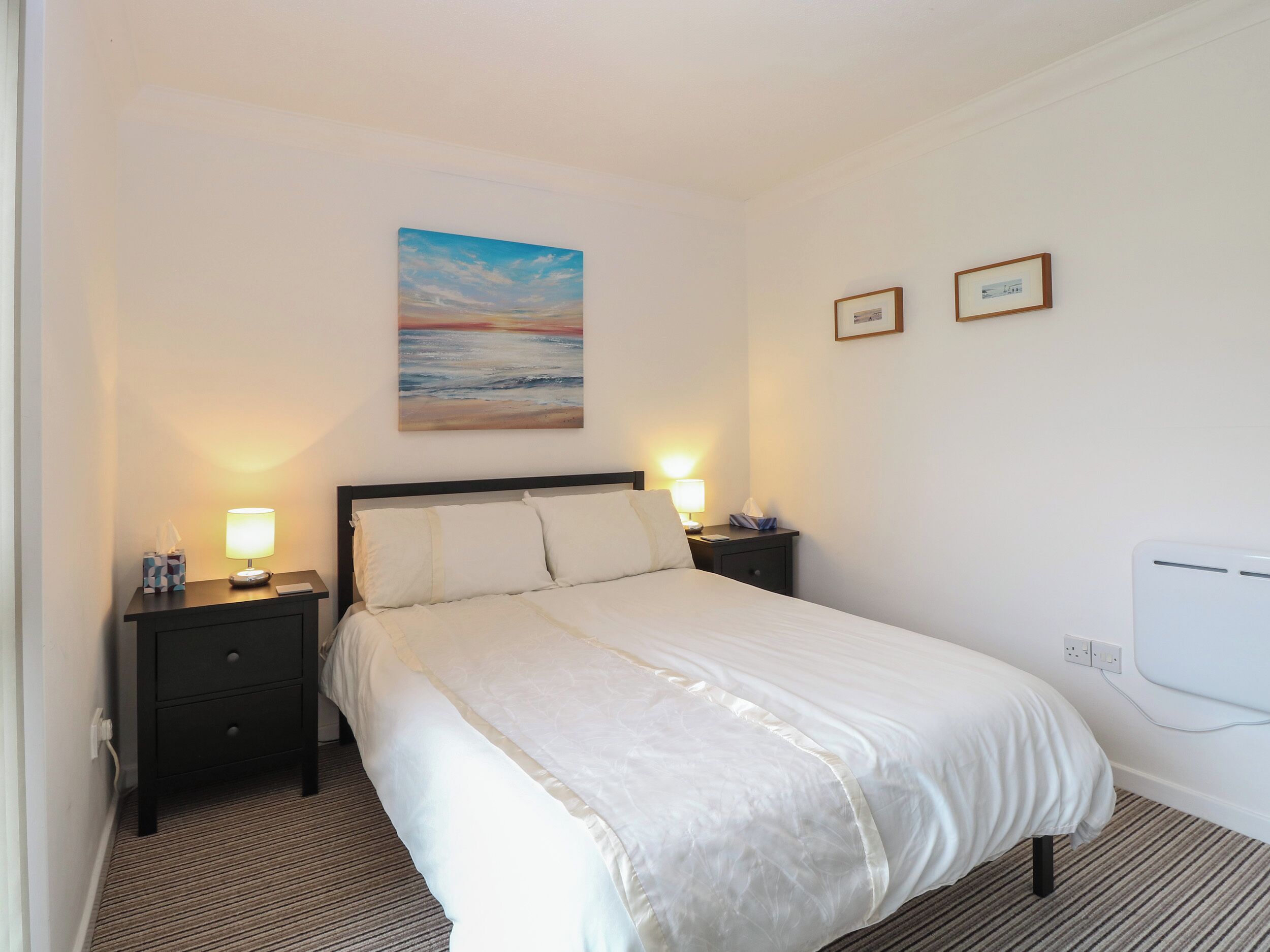 Une chambre d’hôtel avec un lit, deux tables de chevet avec des lampes, un tableau au mur et un climatiseur fixé au mur.