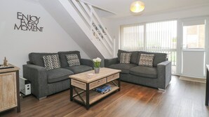 Ein modernes Wohnzimmer mit einer grauen Sofagarnitur, einem Holztisch und einer Treppe mit weißer Geländer.