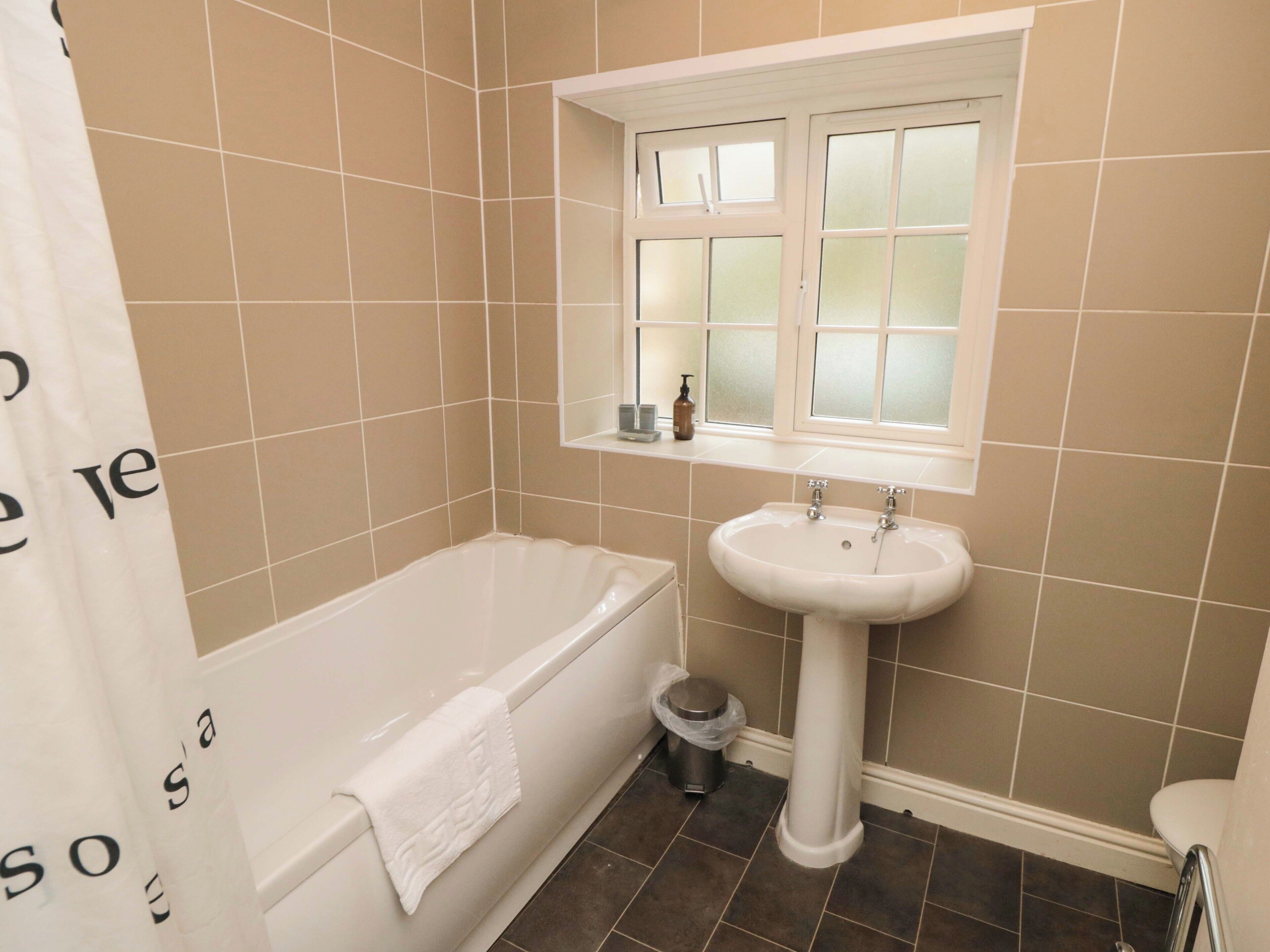 Une salle de bain avec une baignoire, un lavabo, une fenêtre et des toilettes.