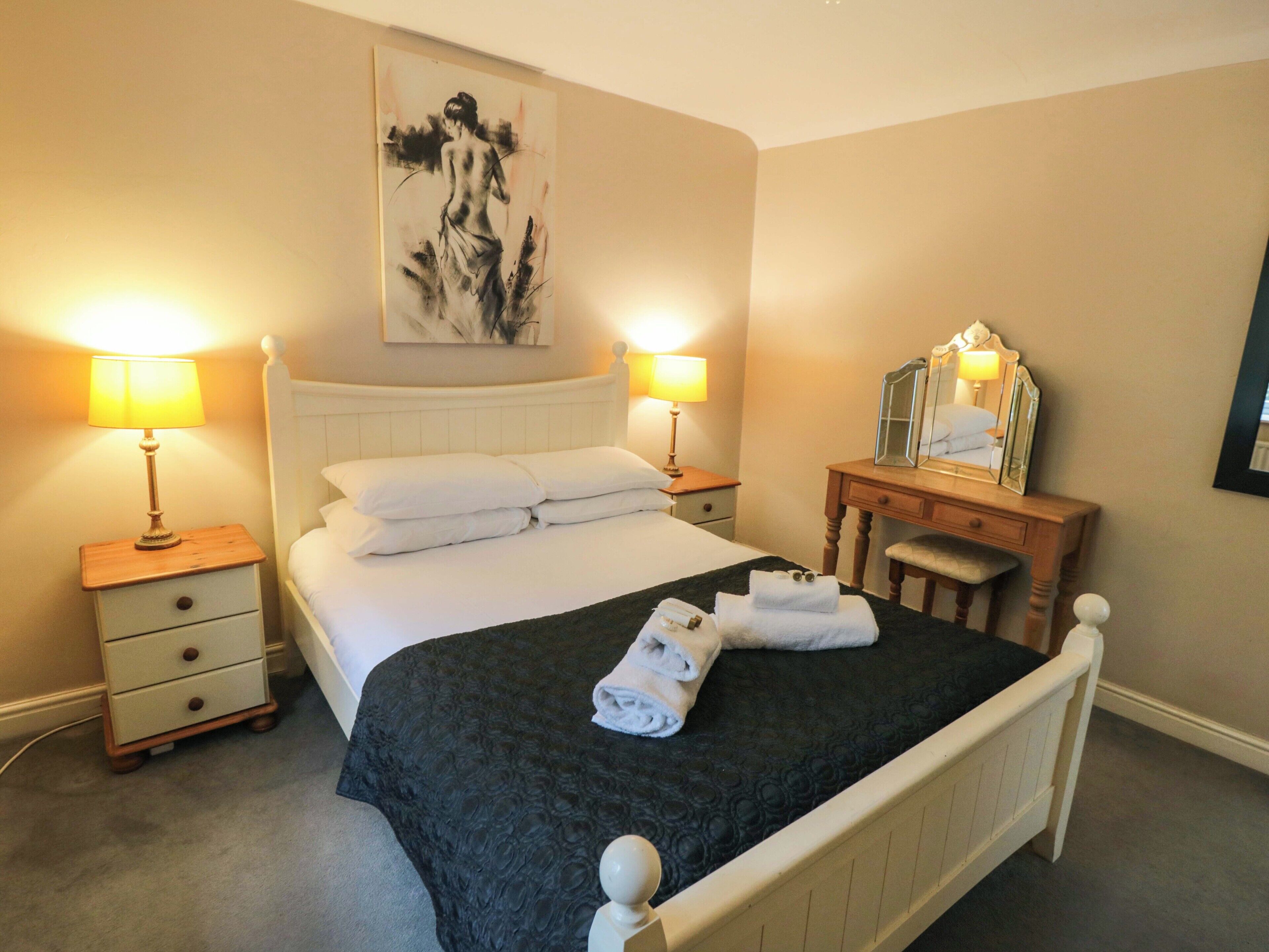 A neatly arranged hotel room with a bed, bedside tables, a dresser, and a painting on the wall.