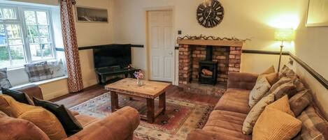 A living room with a fireplace, sofas, a television, and a clock.