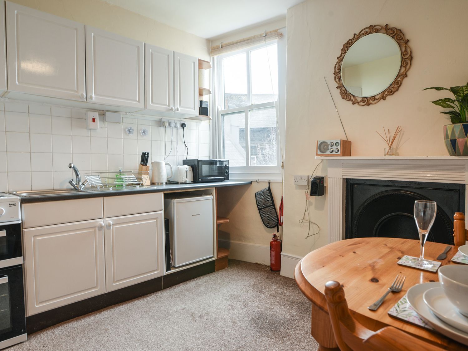 A compact kitchen with white cabinets, a microwave, and a dining area with a wooden table set for two.