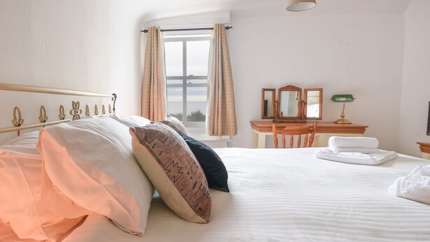 Un lit bien fait, avec des oreillers, un bureau en bois avec un miroir et une lampe.
