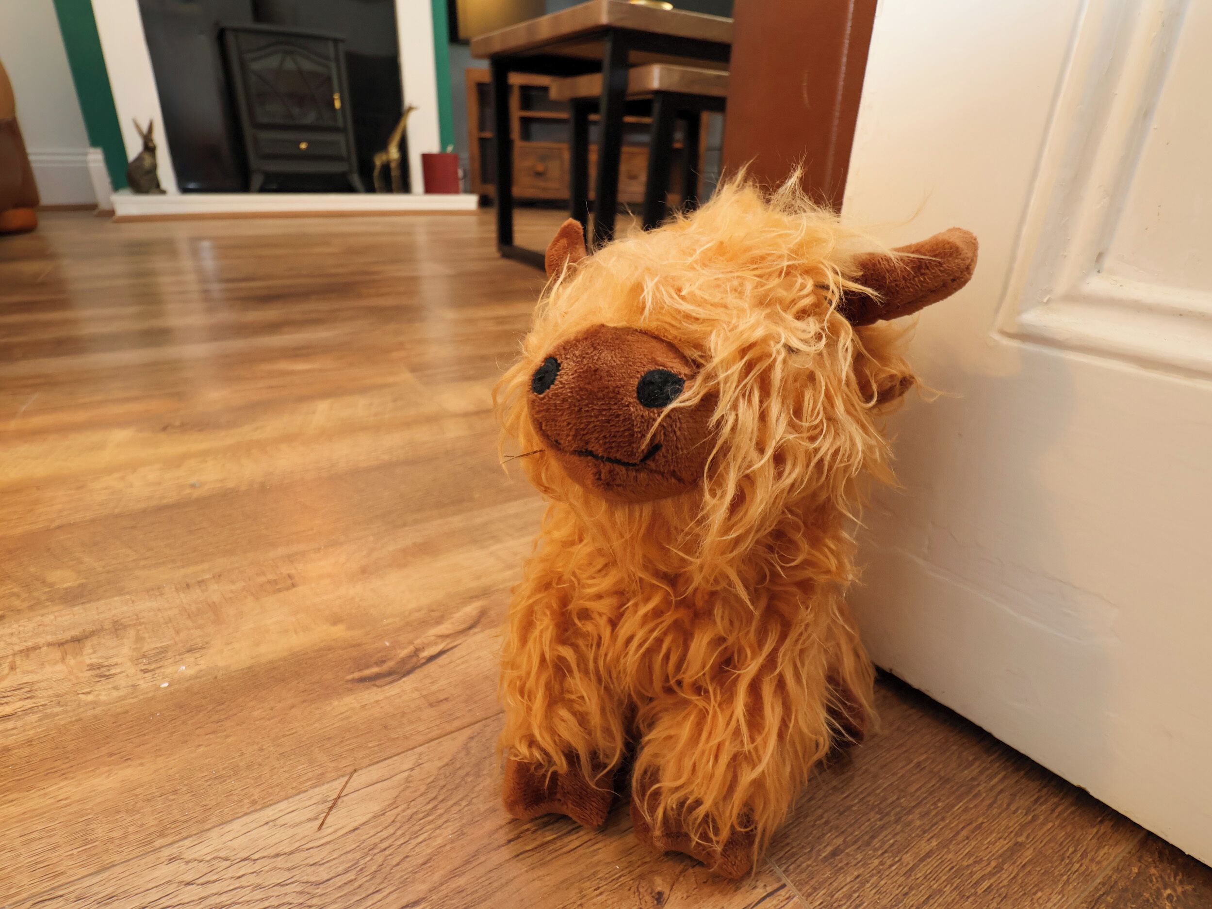 A plush toy resembling a sheep on a wooden floor.