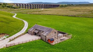 Paisatge rural amb una construcció de pedra, un camí sinuós i un viaducte al fons.