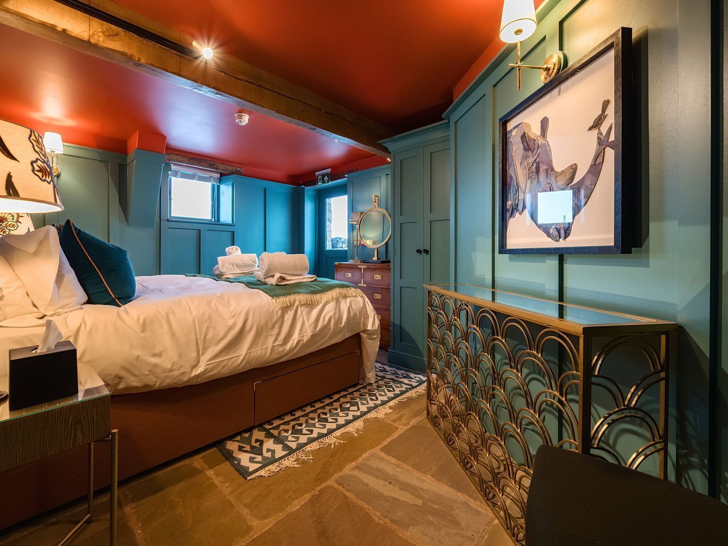 A hotel room with a bed, a desk, a mirror, and a painting on the wall.