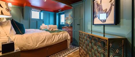 A hotel room with a bed, a desk, a mirror, and a painting on the wall.