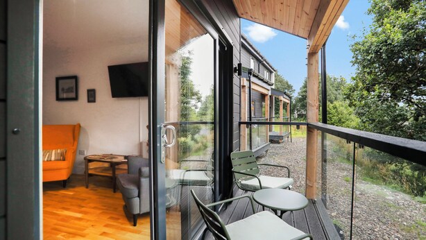A modern interior with a wooden ceiling, a sofa, a TV, and a balcony with outdoor seating. - 26 Strathtay Lodges (Aberfeldy)
