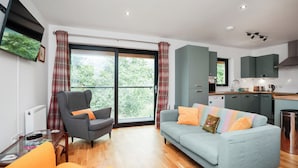A modern living room with a sofa, armchair, and a dining area with a kitchen in the background. - 26 Strathtay Lodges (Aberfeldy)
