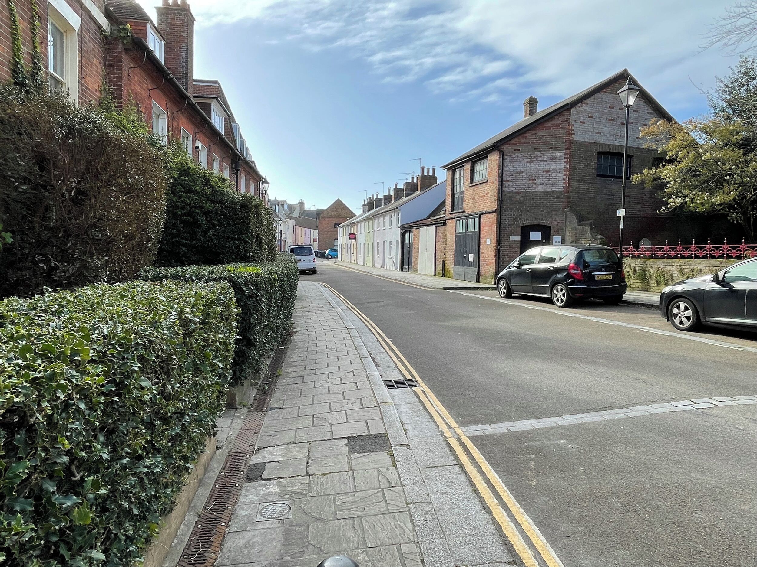 A residential street with brick houses, a sidewalk, and parked cars.