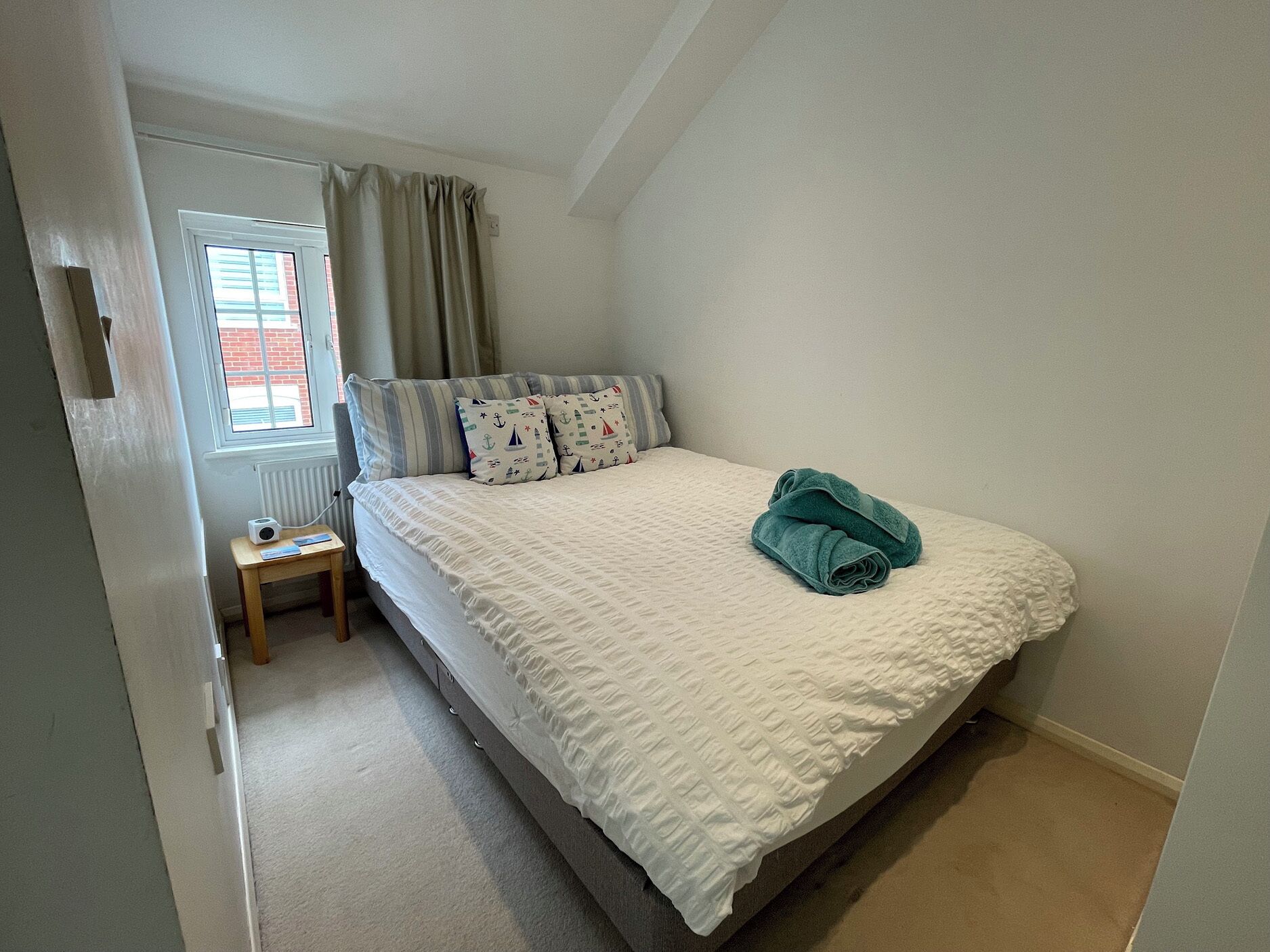 Une chambre à coucher avec un lit, une petite table de chevet, une fenêtre avec des rideaux et un radiateur.