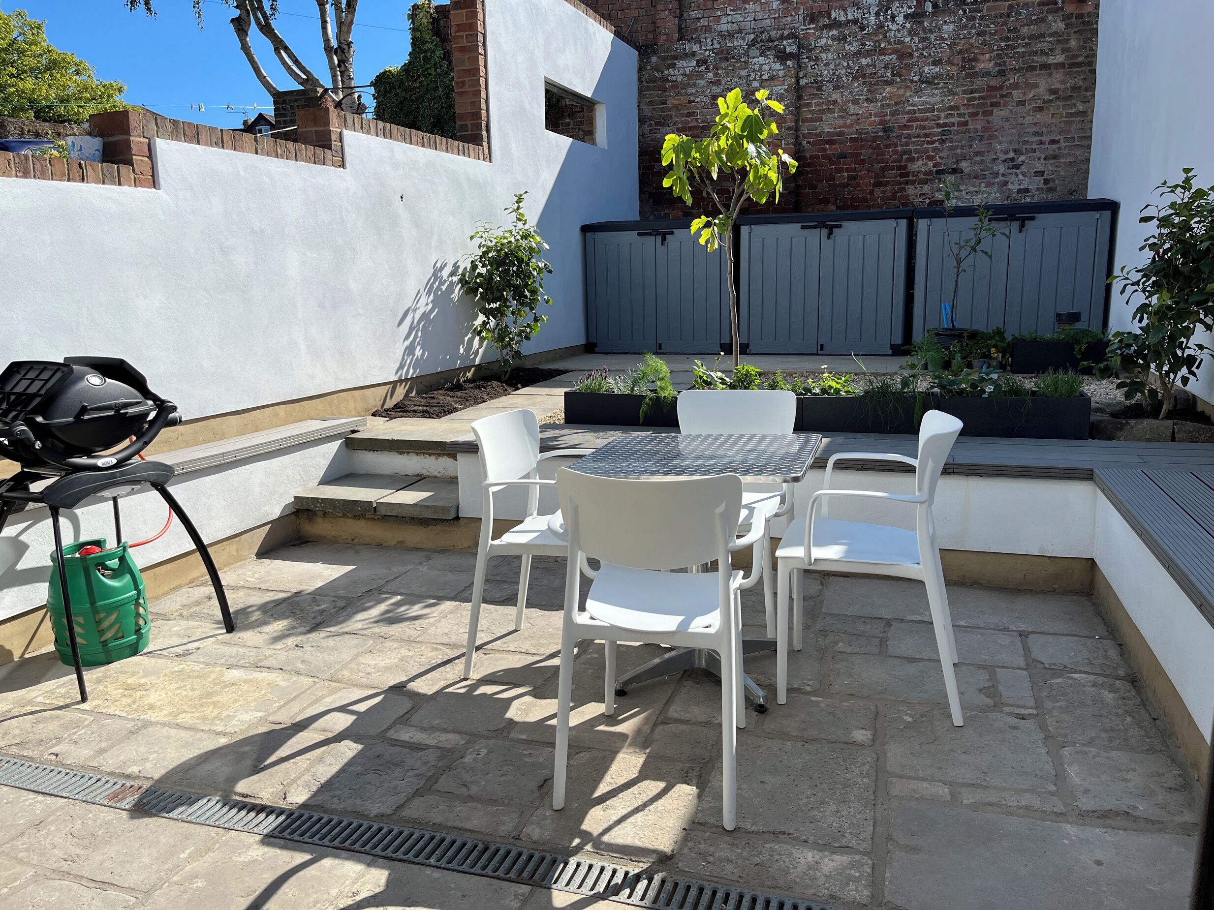 Une terrasse avec un barbecue, des chaises blanches et une table.