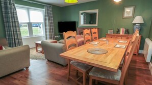 Ein gemütliches Wohnzimmer mit Holzesstisch, Stühlen, einer Couch und einem Fernseher.